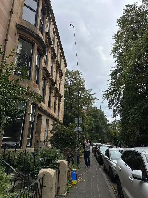 Window cleaner using an extendable pole to reach upper floor windows in Glasgow